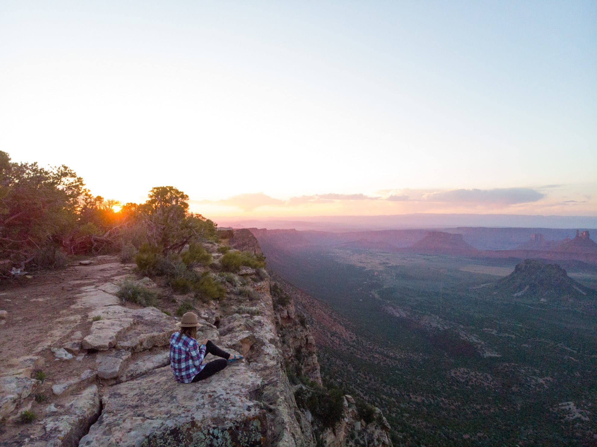 Woman sitting on rocky cliff edge in Utah at sunset with Canyonland vistas below