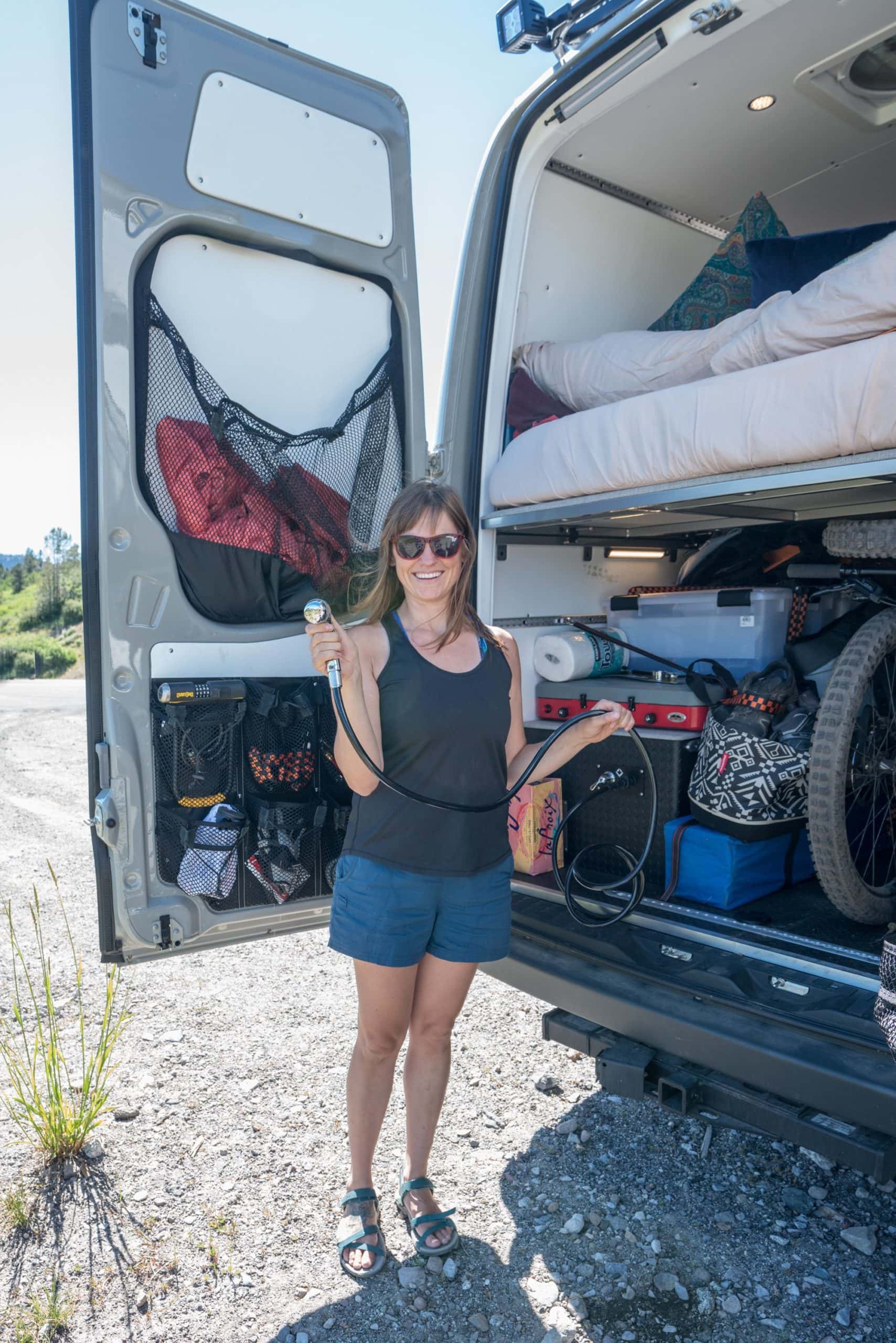 Woman standing at back of converted Sprinter van holding a showerhead