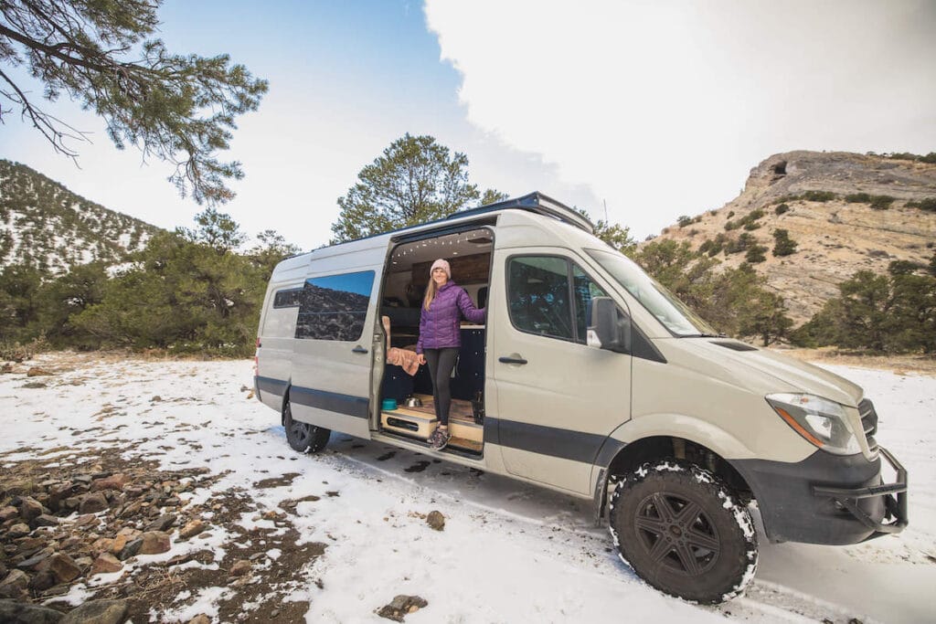 Kristen standing in open doorway of her Sprinter van looking out onto winter landscape in Colorado