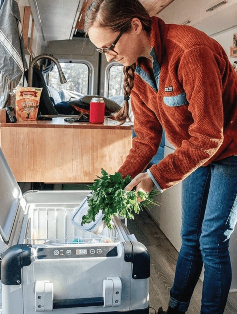 Woman taking parsley out of chest-style campervan fridge in converted van