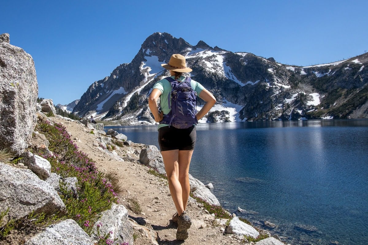 Kristen Bor hiking next to a blue alpine lake wearing the Osprey Raven 10 backpack in purple