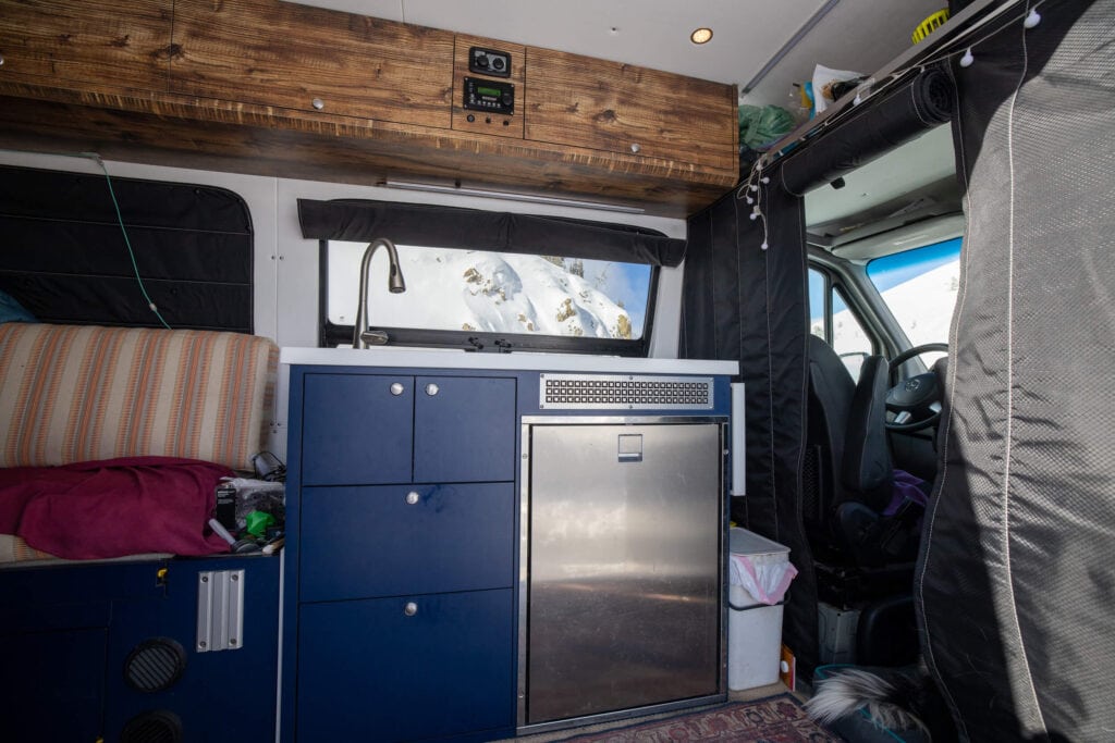 Van kitchen area with cabinets and campervan fridge behind drivers seat