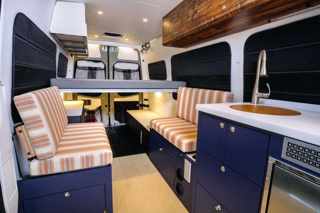 Inside a Sprinter camper van with a fixed bed, seating area, and galley for a great van layout