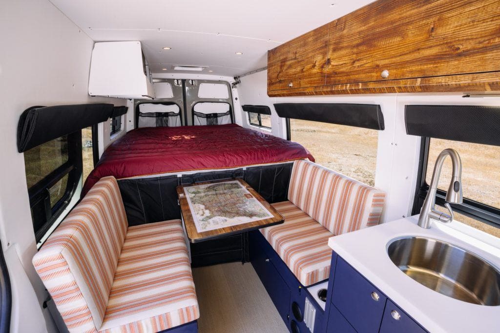 Interior of converted camper van with bed in rear and two bench seats facing a table