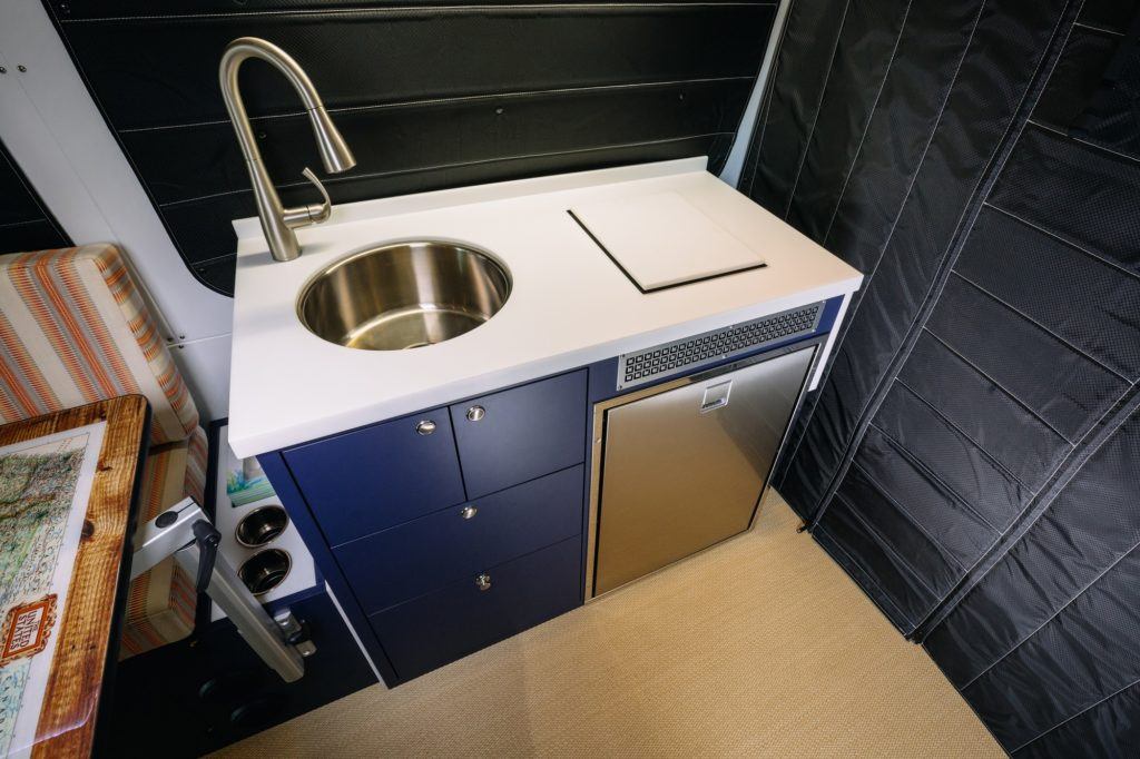 Converted van kitchen area with sink and faucet, cabinets, and white counterspace