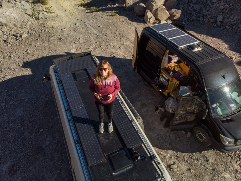 woman standing on the roof of a Sprinter van holding a drone controller