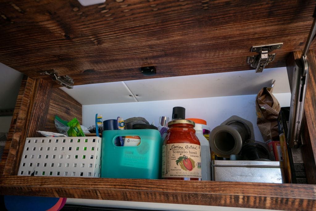 a closeup of the inside of a van cabinet showing storage bins, toiletries, and pantry items