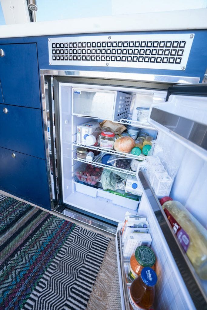 Campervan fridge with door open showing variety of food and beverages