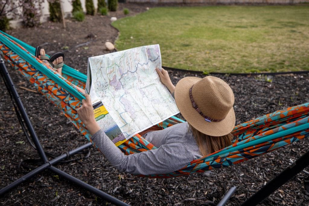 A woman lays in a printed ENO doublenest hammock looking at a map
