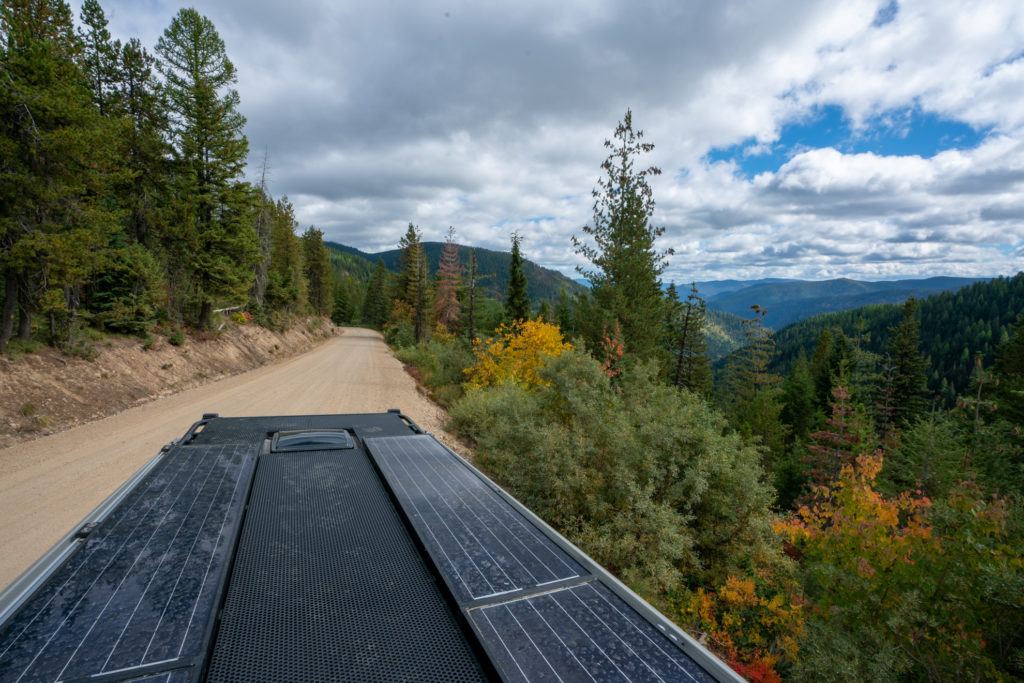 top of a Sprinter van with solar panels on a dirt road with fall colors in the background