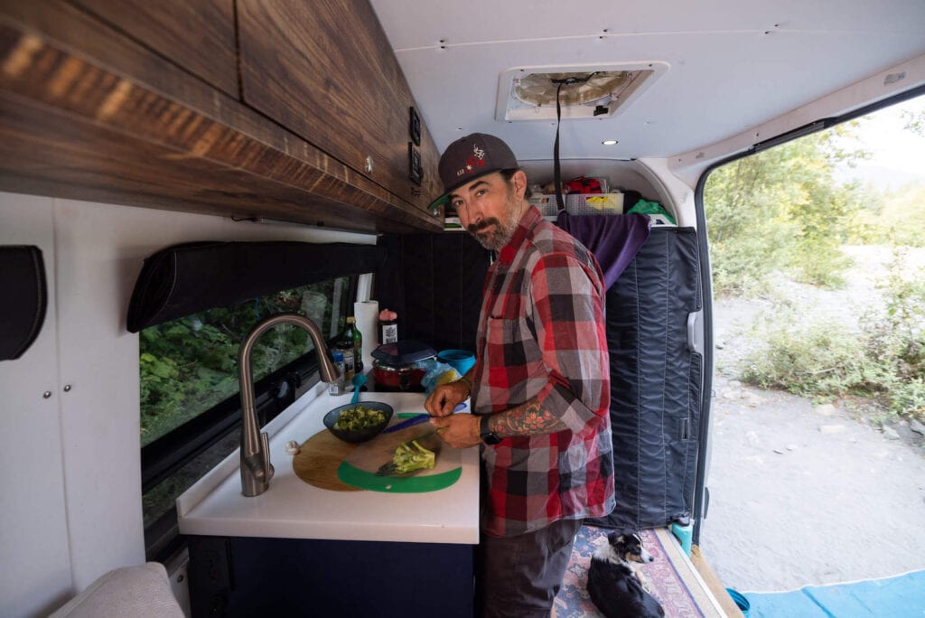 Ryan prepping vegetables for meal on kitchen counter in converted Sprinter Van