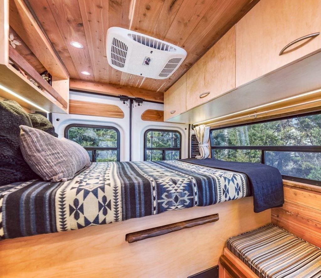 the interior of a campervan close up to a bed with a printed comfortable and upper van cabinets above the bed