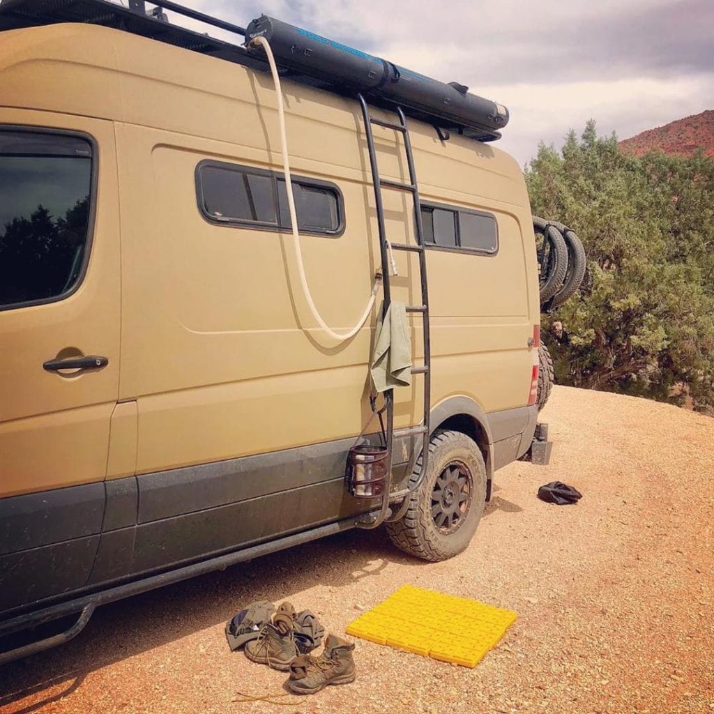 A tan Sprinter van with a black tube attached to the top of a van for a portable road shower