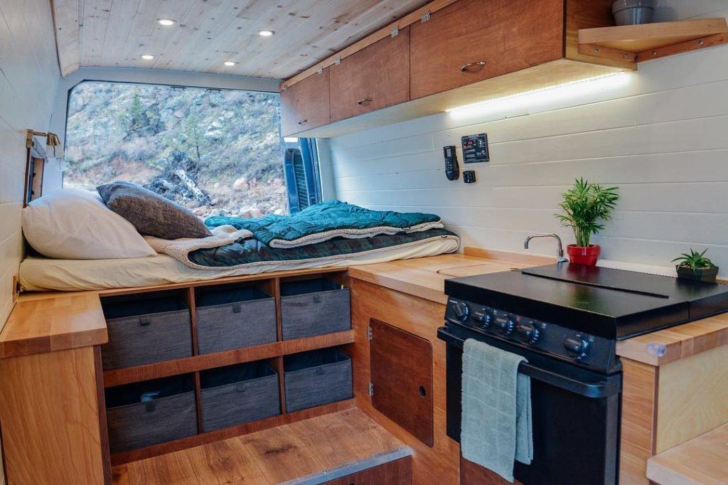 the interior of a campervan with an oven, fixed bed, and fabric storage bins under the bed