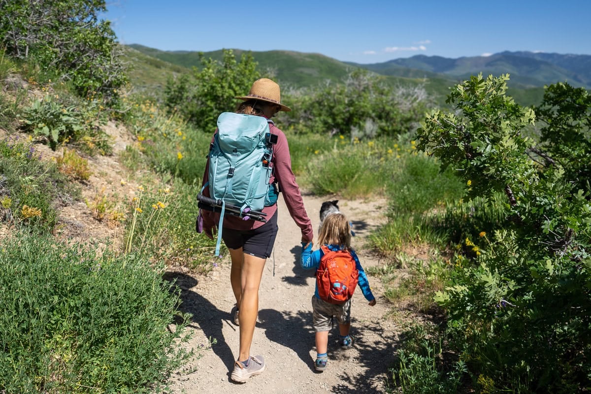 Kristen Bor wearing the Deuter Trail 28 SL backpack on a trail in Park City with green foliage next to her 2 year old son