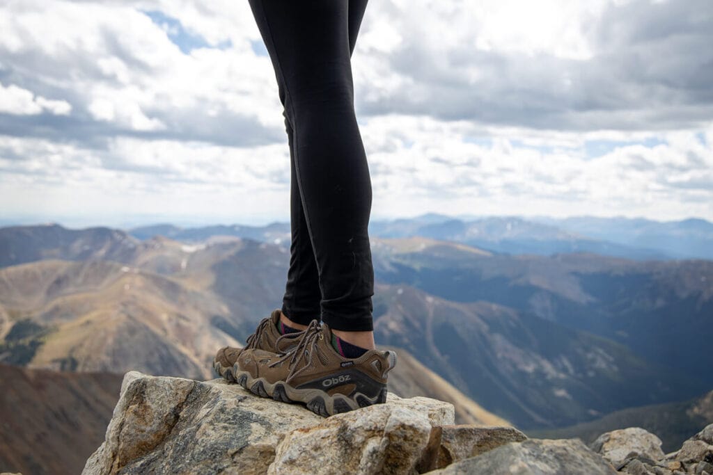 Close up photo of women wearing Oboz hiking shoes standing on rocky overlook on hike in Colorado