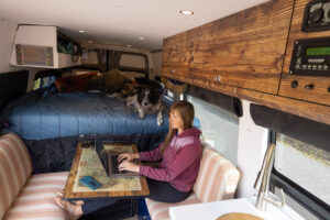 woman sitting at a Lagun table working on a laptop in her campervan with a fixed bed in the background