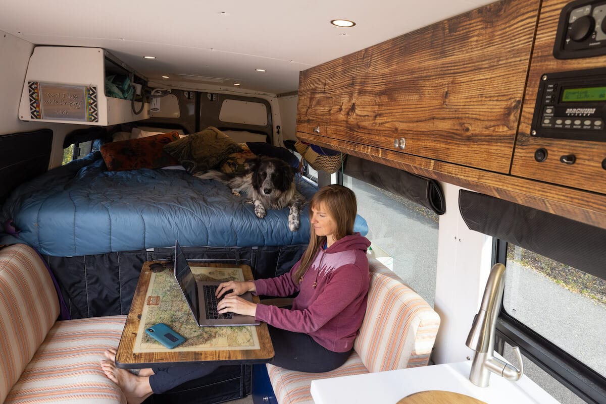 woman sitting at a Lagun table working on a laptop in her campervan with a fixed bed in the background