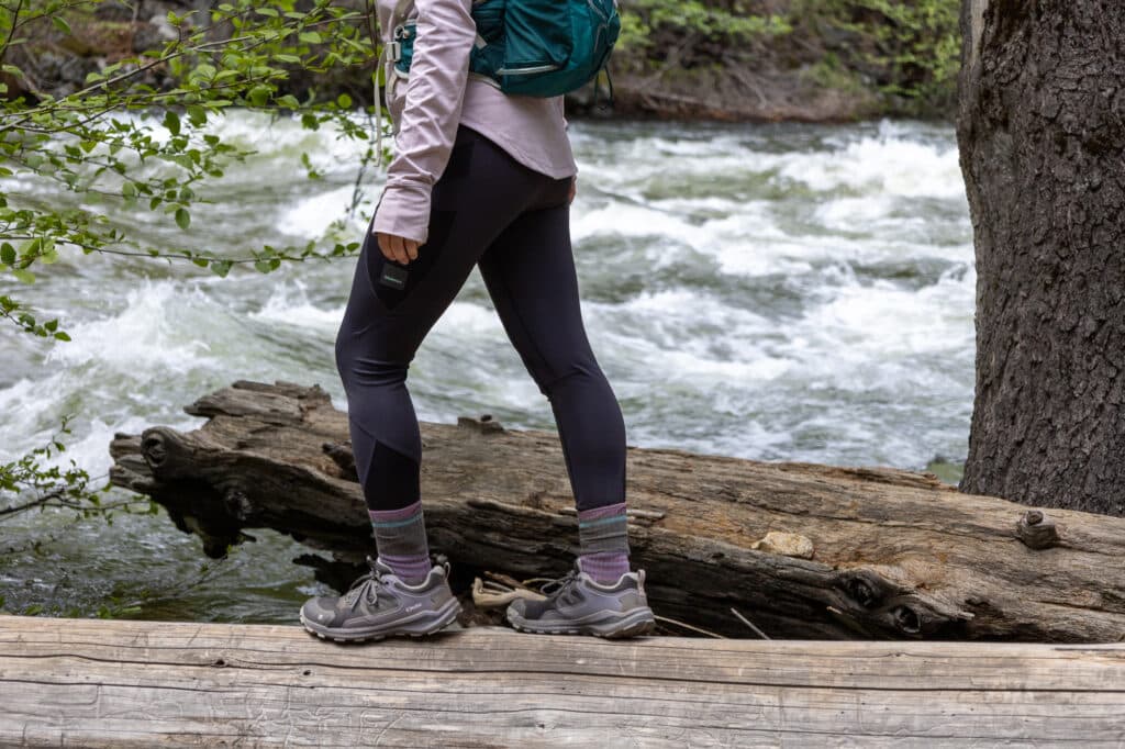 Women hiking on log above a river wearing the Oboz Katabatic hiking shoe