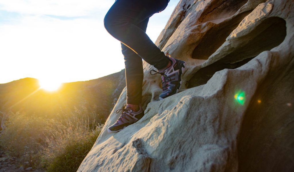 Photo of women's legs hiking down rock face as sun sets in the background