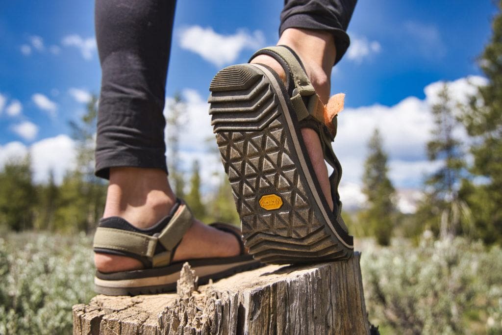 Close up photo of sole of Teva Universal Trail sandal worn by woman standing on tree stump in meadow