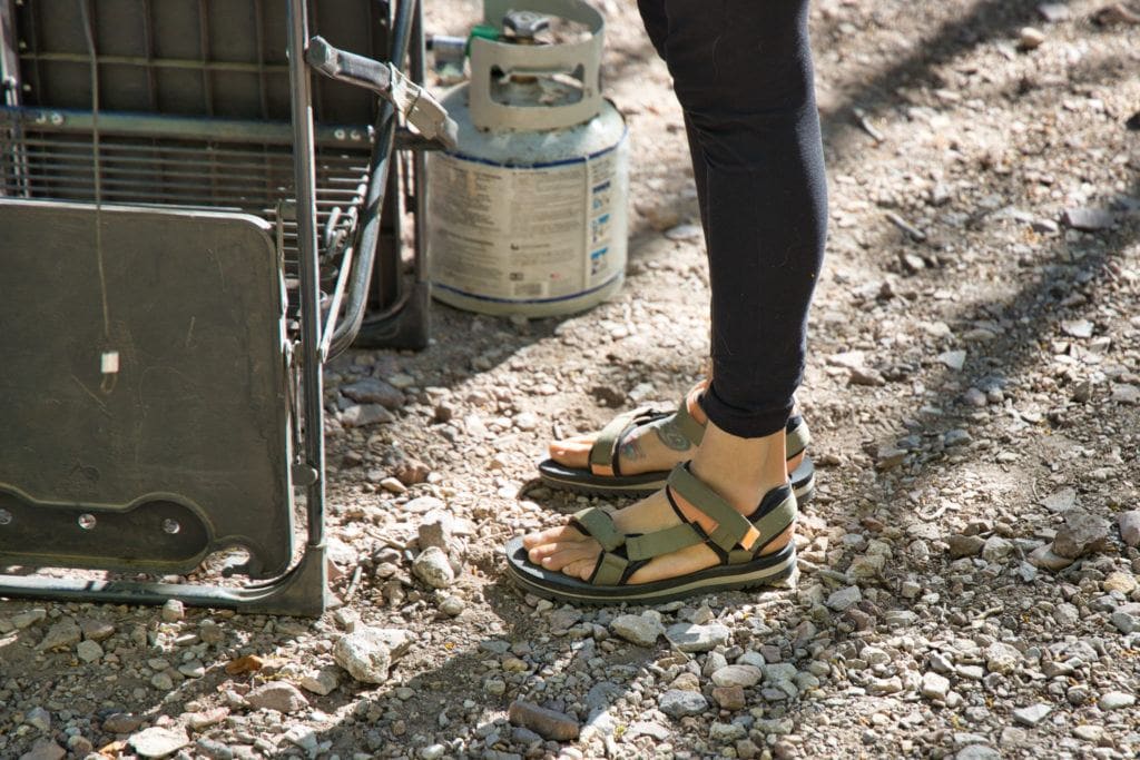 Close up shot of woman wear Teva Universal Trail Sandals standing on gravel surface next to camp grill