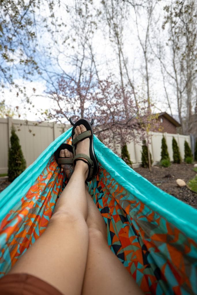 Photo out over legs of woman lying in a hammock wearing Teva Universal Trail sandals in backyard