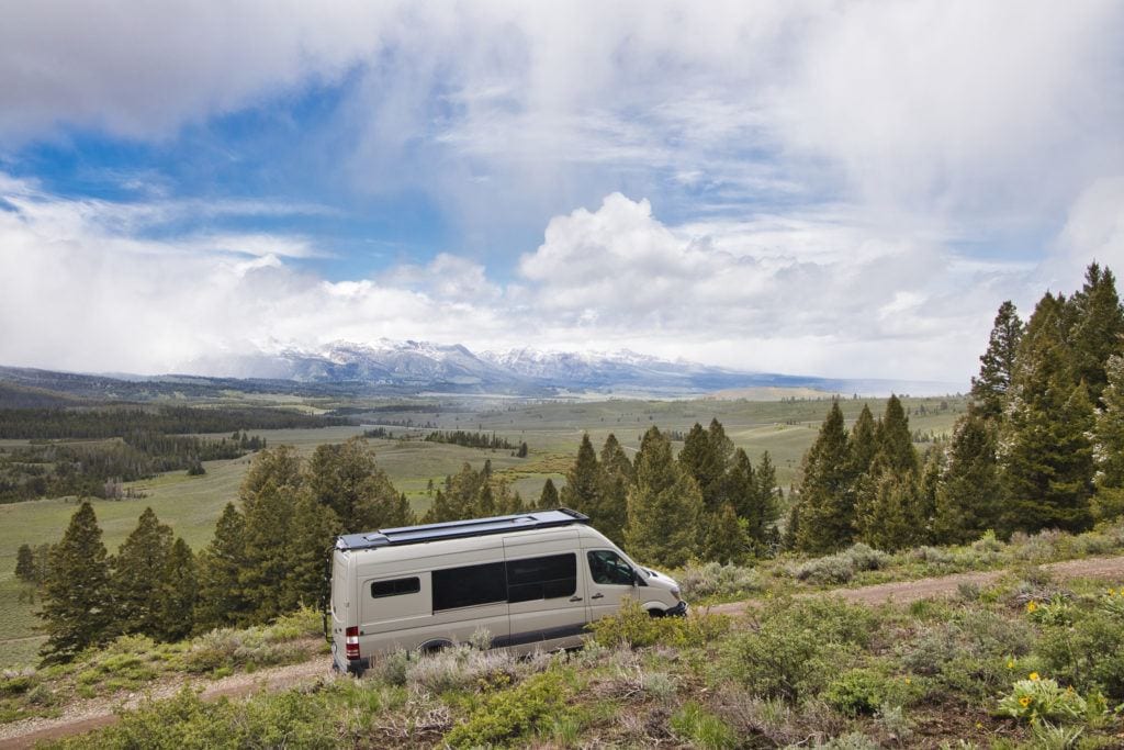 A Sprinter van drives up a dirt road with mountains in the distance