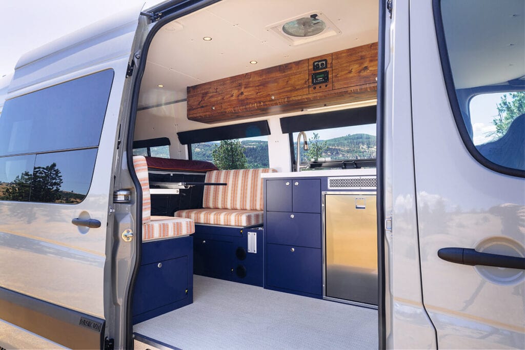 Interior view of a converted Sprinter camper van through sliding door showing the kitchen and seating area