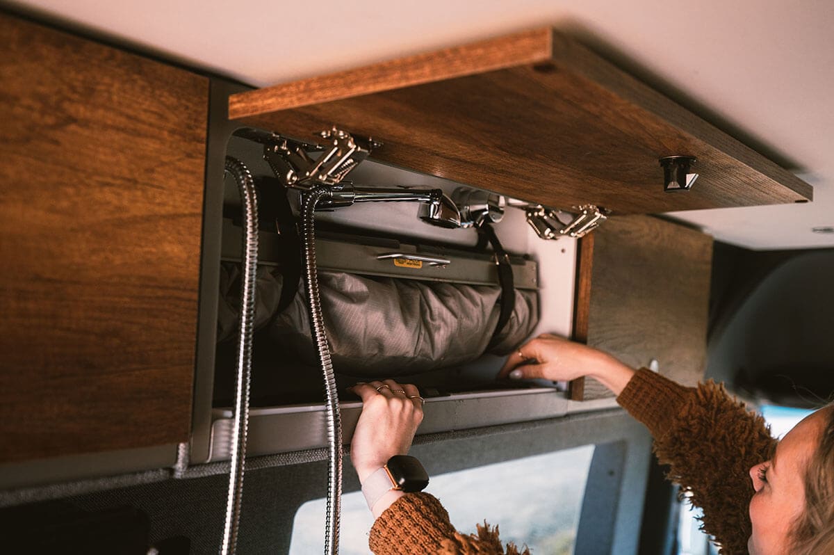 person reaching into an upper cabinet with a foldable Storyteller shower setup