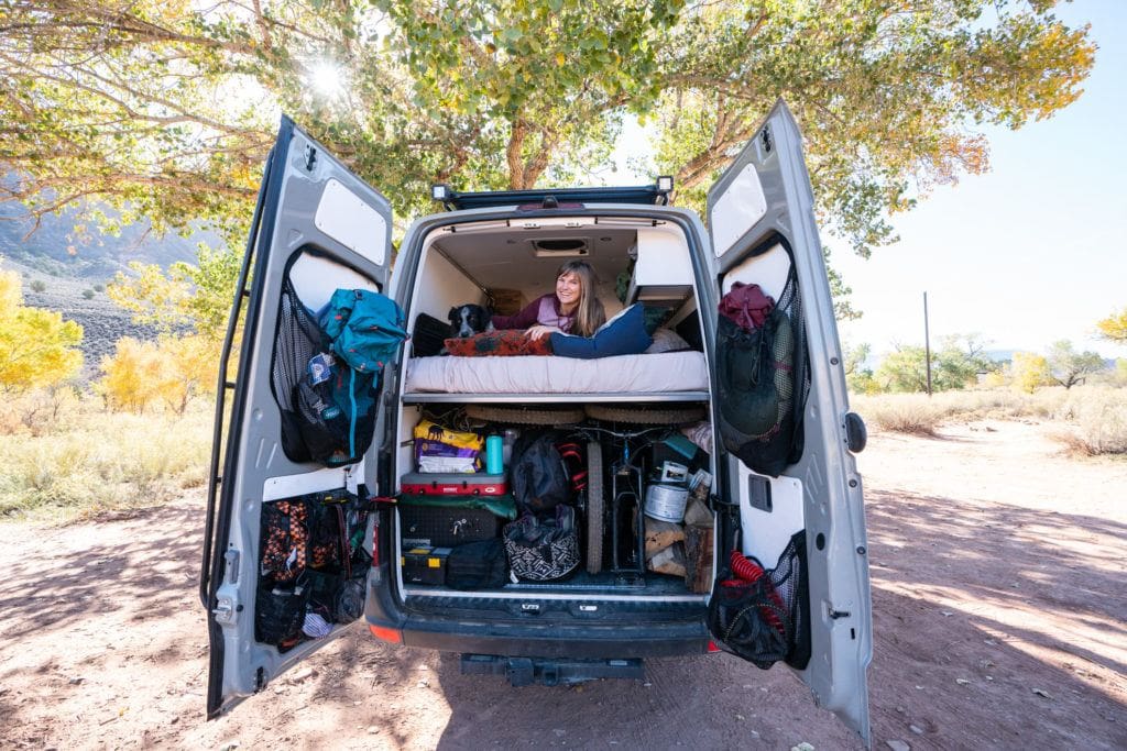 Bearfoot Theory founder Kristen Bor lying in the bed in her Sprinter Van with the back doors open