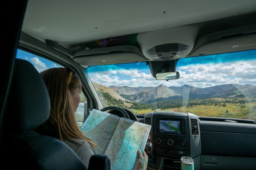 A woman uses a road atlas to find a free campsite