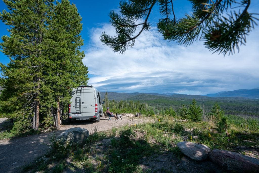 A man sits outside of a Sprinter van while free camping near Grand Lake in Colorado