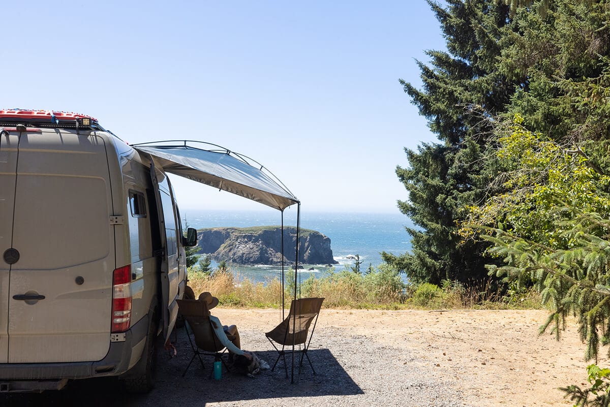 Van with awning out and Kristen Bor sitting under awning at scenic overlook on Oregon Coast