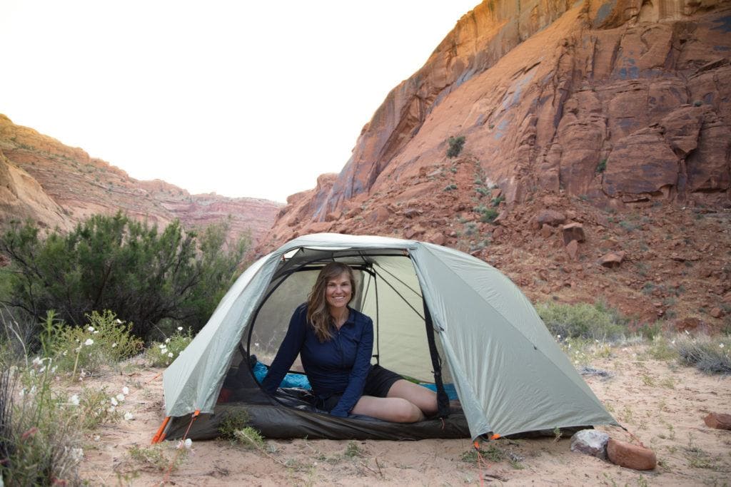 A woman sitting inside her REI Co-op Quarter Dome SL 2 Tent backpacking in the desert