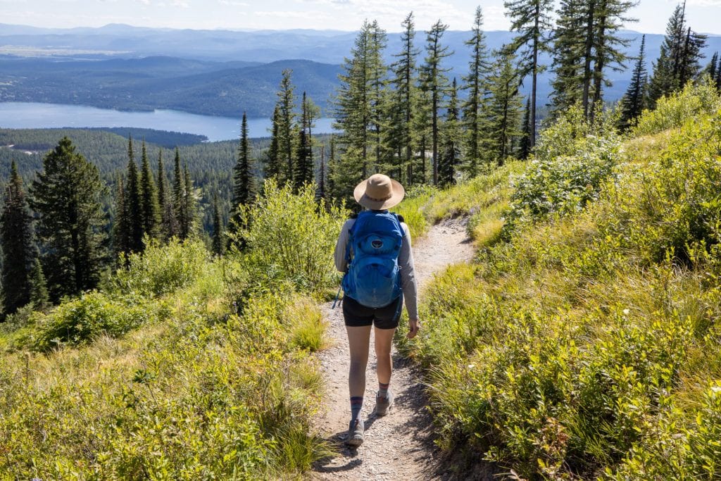 Mulher caminhando longe da câmera na trilha com vista para um lago e montanhas