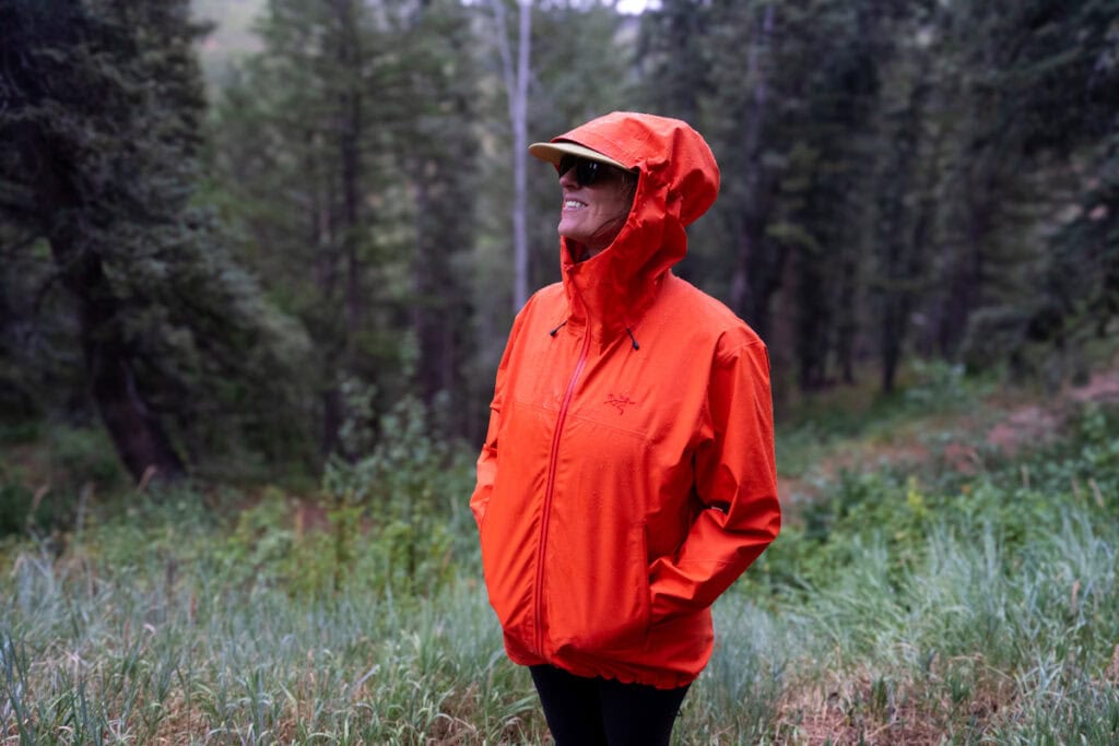 Kristen Bor wearing a red Arc'teryx Beta SL Rain Jacket on during a rainy hike. She is zipping up the zipper