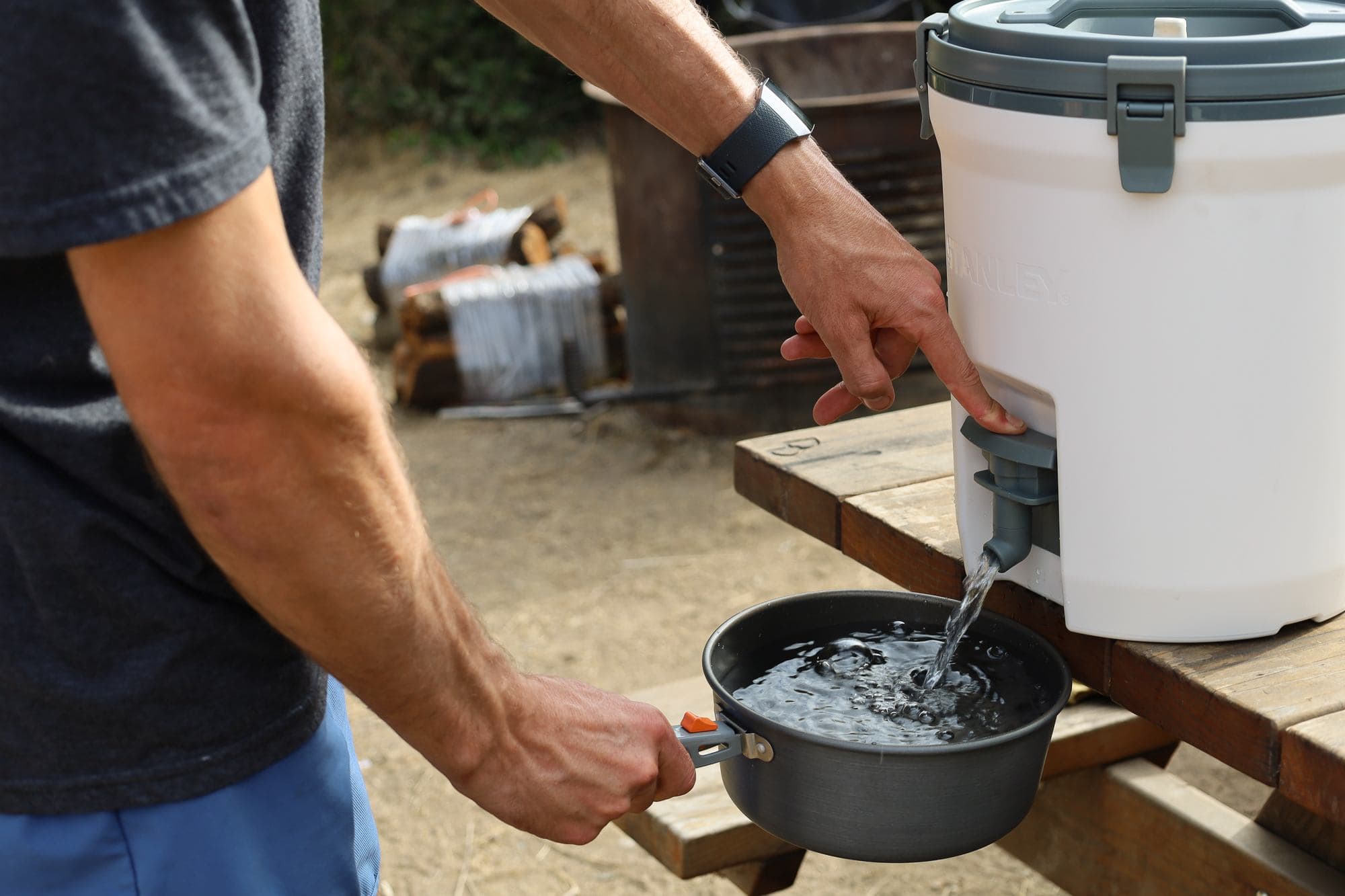 A man pouring water from a reusable, refillable water jug into a pot at a camp table