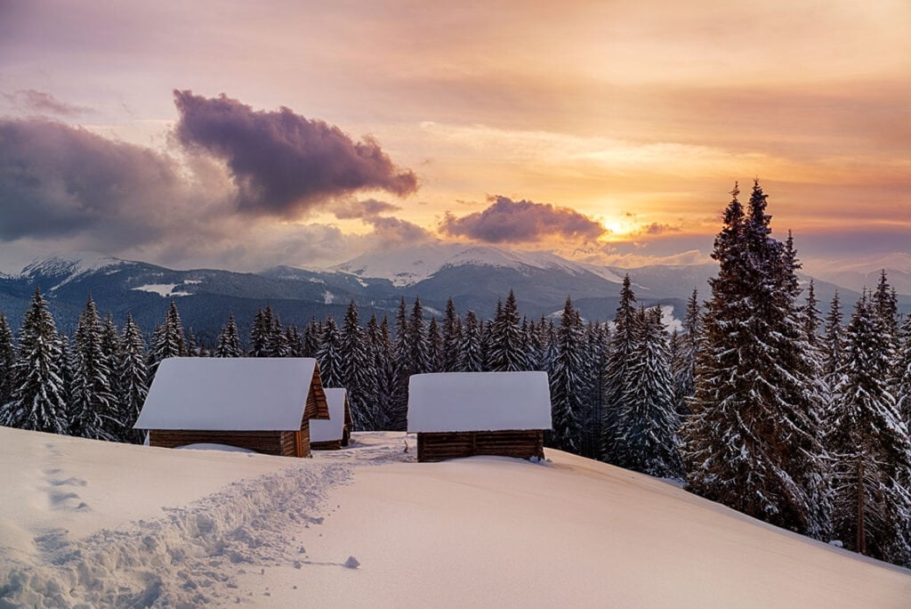 Winter huts in snowy landscape at sunset