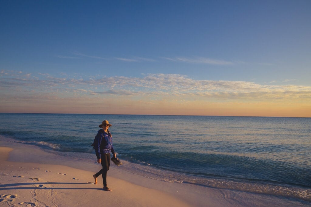 Kristen walking barefoot along a sandy beach at sunset