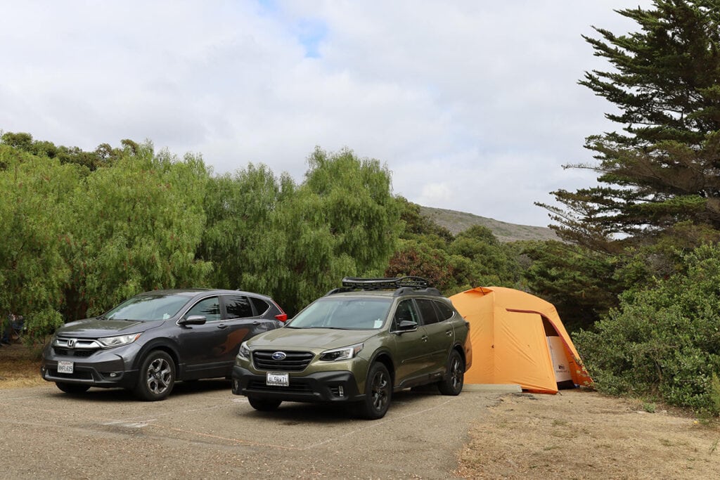 Two cars parked next to an orange tent while car camping