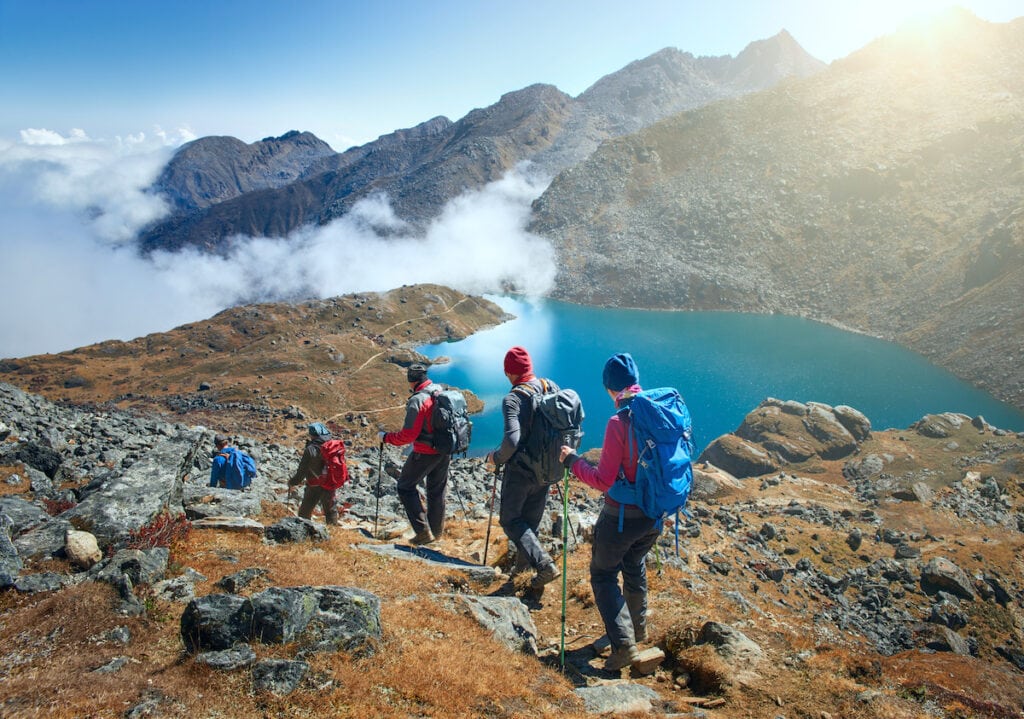 Group of hikers descending alpine trail with views of mountains and lake