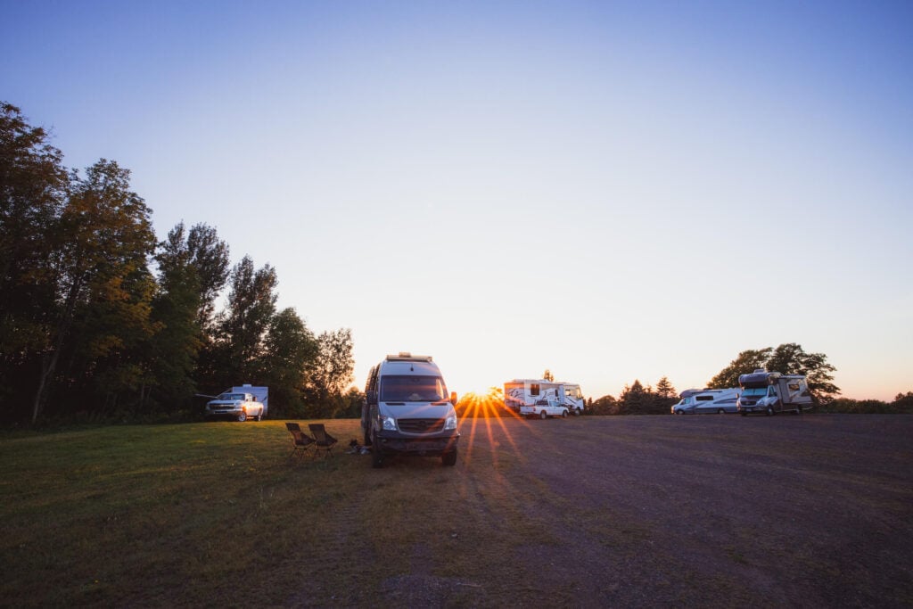 Multiple vans and RVs are parked in a field at a Harvest Host location at sunset