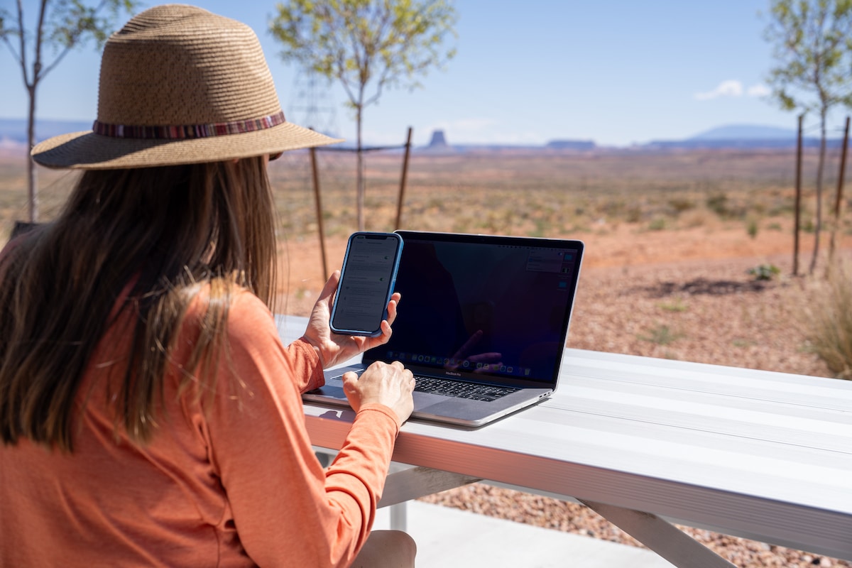 Kristen Bor with a laptop and her phone in her hand sitting at a picnic table