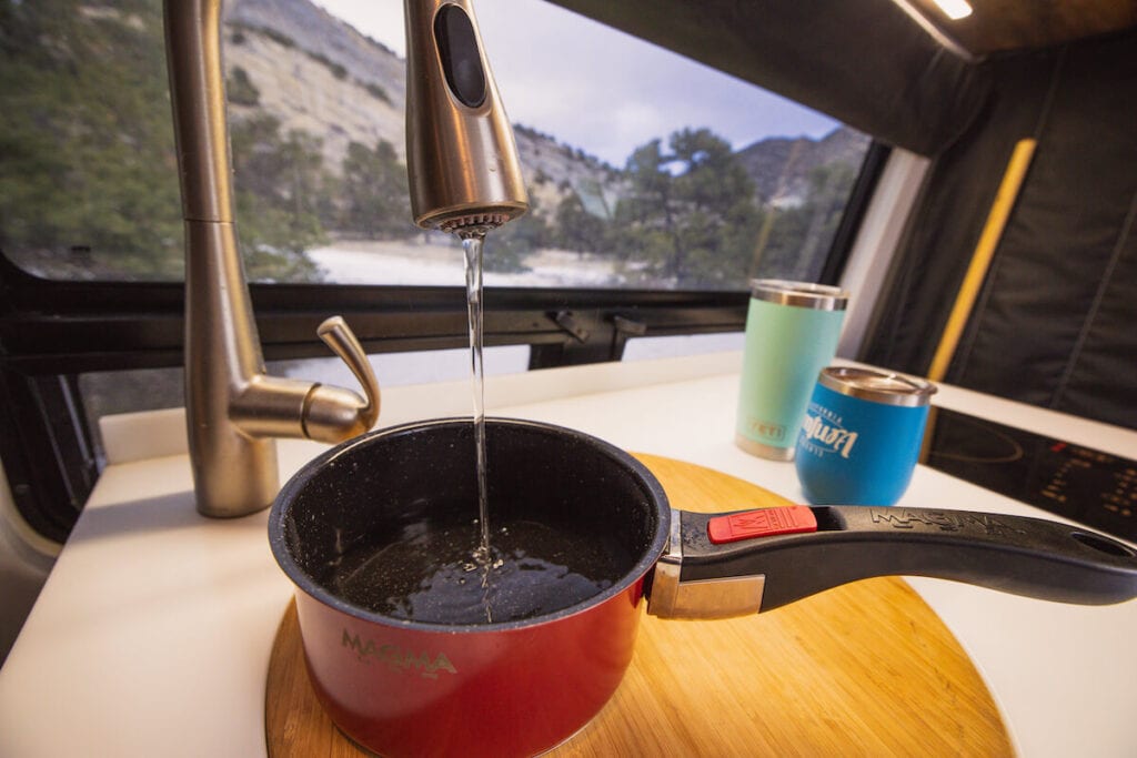 A small pot of water is filling from a sink inside a Sprinter Van