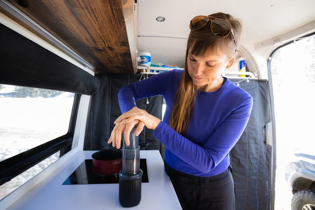 A woman making coffee in her Sprinter van with an Aeropress Go coffee press