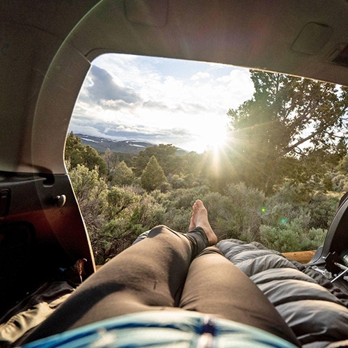 Point of view from a woman lying in the back of a Subaru looking at the sunset over the forest