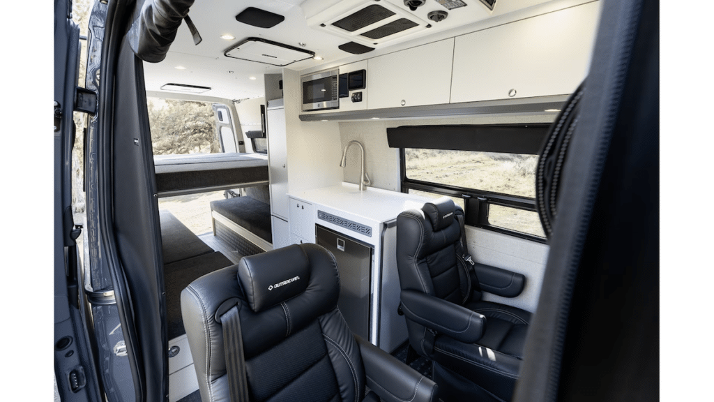 Inside of Outside Van's Approach Model Van. Photo shows two captains chairs designed for passengers with a galley, platform bed and a convertible dinette - all inside a 170" Sprinter van