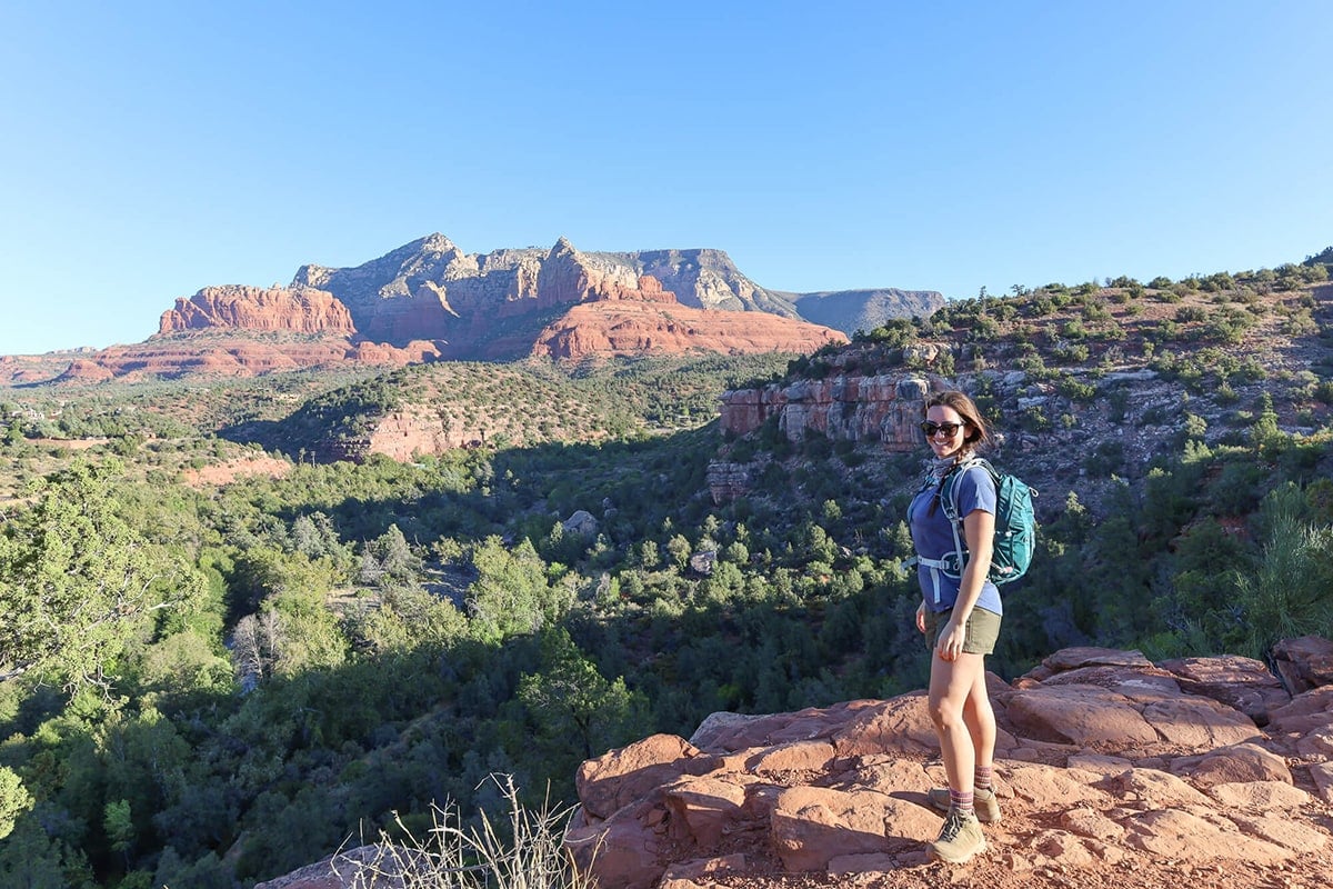 Female hiker standing at lookout on trail in Sedona surrounded by red rock bluffs and forest