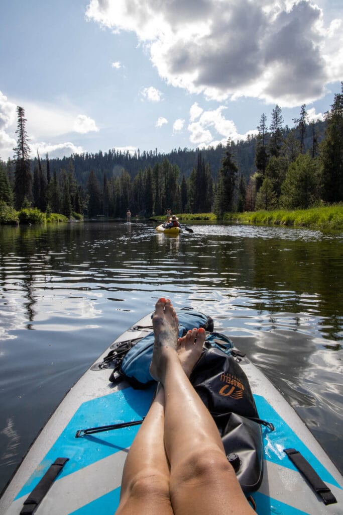 Relaxing on a paddle board with packrafter ahead in the river